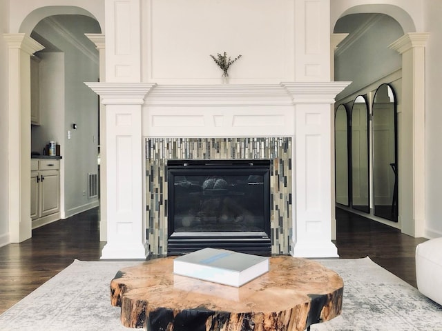 details with ornamental molding, a glass covered fireplace, ornate columns, and wood finished floors