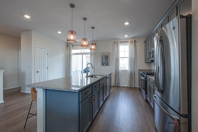 kitchen featuring a center island with sink, a breakfast bar, appliances with stainless steel finishes, dark wood-style floors, and a sink