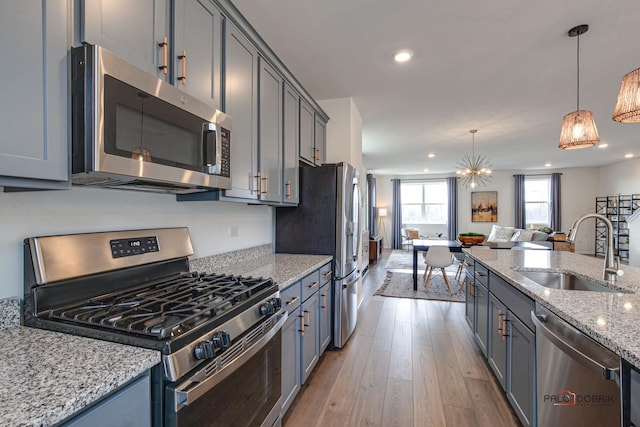 kitchen featuring light stone counters, wood finished floors, a sink, stainless steel appliances, and open floor plan