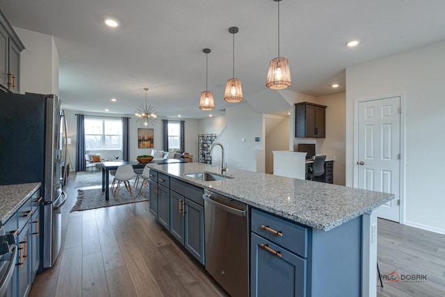 kitchen with a sink, light stone counters, open floor plan, dark wood-style floors, and stainless steel appliances