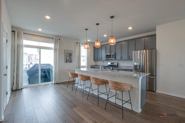 kitchen with a breakfast bar, a center island with sink, light stone counters, dark wood-style floors, and appliances with stainless steel finishes