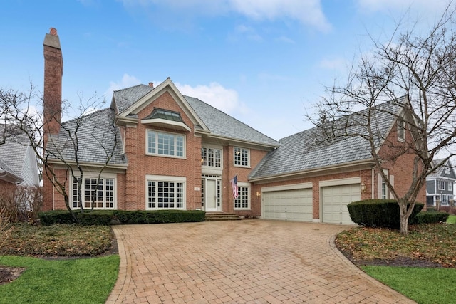 view of front of house with a high end roof, an attached garage, brick siding, and a chimney