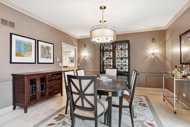 dining space featuring visible vents, a decorative wall, an inviting chandelier, wainscoting, and crown molding