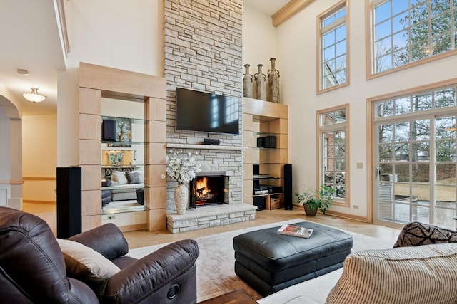 living area with wood finished floors, baseboards, arched walkways, a stone fireplace, and a towering ceiling