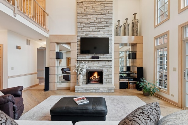 living room with a stone fireplace, wood finished floors, visible vents, and baseboards