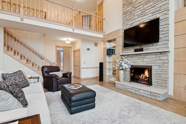 living room featuring a stone fireplace, stairway, a towering ceiling, and wood finished floors