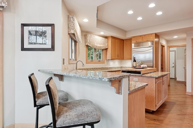 kitchen with light wood-type flooring, stainless steel built in refrigerator, a kitchen breakfast bar, recessed lighting, and a peninsula