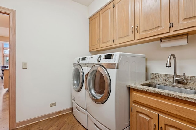 laundry area featuring baseboards, washing machine and clothes dryer, light wood-style flooring, cabinet space, and a sink