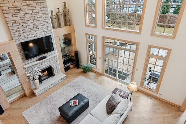 living area featuring visible vents, a high ceiling, a stone fireplace, and wood finished floors