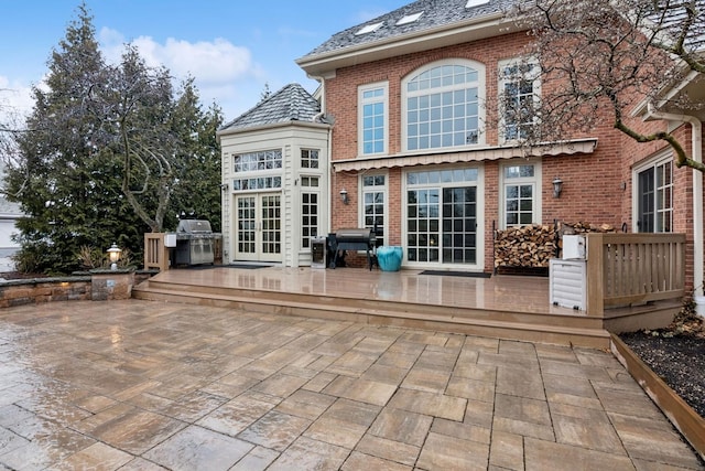 rear view of property with a deck, a patio, french doors, and brick siding