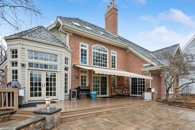 rear view of house with a wooden deck, french doors, brick siding, and a chimney