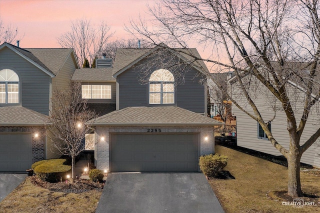 view of front facade with roof with shingles, a chimney, a garage, aphalt driveway, and brick siding