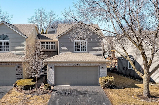 traditional home with driveway, a chimney, a shingled roof, a garage, and brick siding