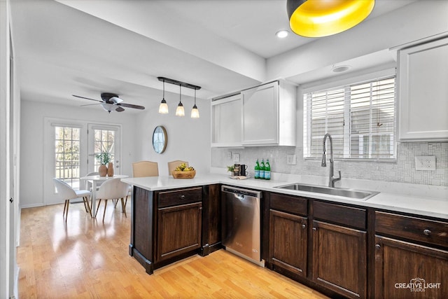 kitchen with a peninsula, a sink, decorative backsplash, light countertops, and dishwasher