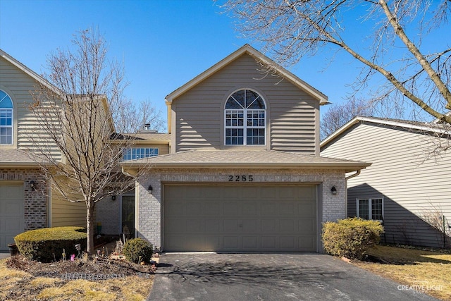 traditional home with a garage, brick siding, driveway, and a shingled roof