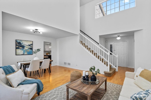 living area featuring visible vents, baseboards, stairway, a towering ceiling, and wood finished floors