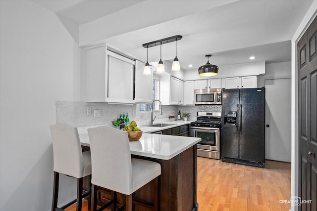 kitchen featuring backsplash, white cabinetry, a peninsula, stainless steel appliances, and a sink