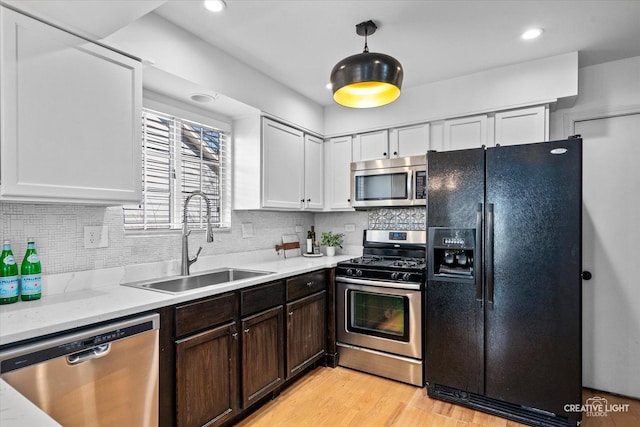 kitchen featuring a sink, appliances with stainless steel finishes, white cabinetry, light wood-type flooring, and backsplash