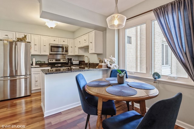 kitchen featuring a peninsula, white cabinets, light wood finished floors, and stainless steel appliances