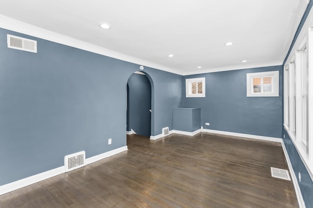 empty room with visible vents, arched walkways, and wood finished floors