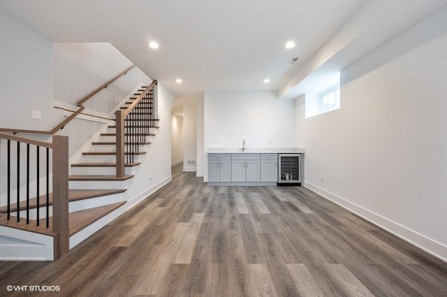 interior space featuring indoor wet bar, a sink, wood finished floors, beverage cooler, and baseboards