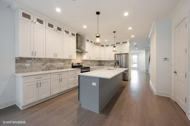 kitchen with a sink, appliances with stainless steel finishes, wall chimney range hood, and white cabinetry