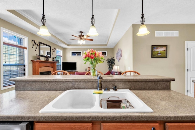 kitchen featuring a tray ceiling, a fireplace, visible vents, and a sink