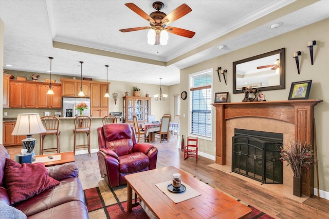 living room with a raised ceiling, a textured ceiling, light wood-style flooring, and crown molding