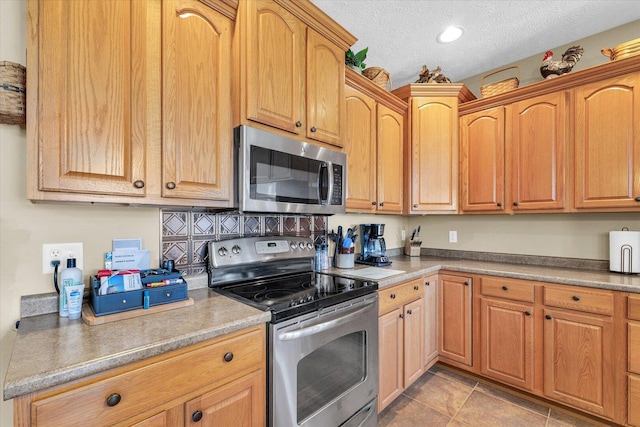 kitchen with light countertops, light tile patterned floors, recessed lighting, appliances with stainless steel finishes, and a textured ceiling