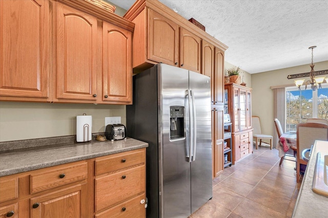 kitchen with a notable chandelier, stainless steel refrigerator with ice dispenser, a textured ceiling, dark countertops, and brown cabinetry