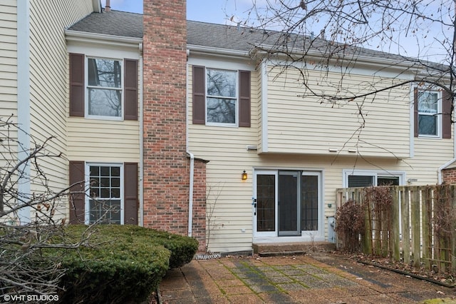 back of property with brick siding, a chimney, a shingled roof, a patio area, and fence