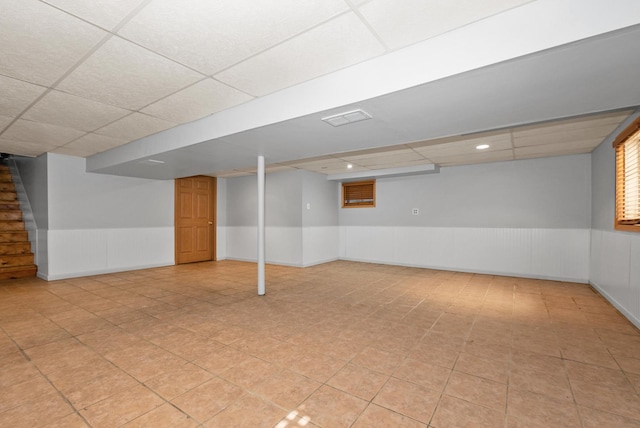 finished below grade area with stairs, a wainscoted wall, and a drop ceiling