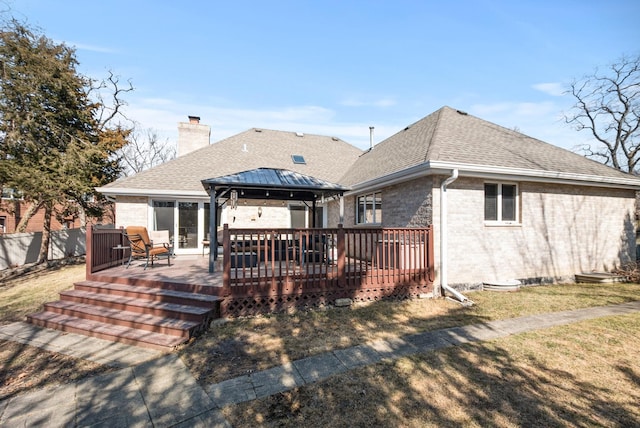 back of property with a wooden deck, a chimney, a shingled roof, a gazebo, and brick siding