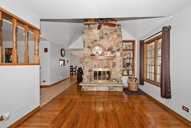 unfurnished living room featuring visible vents, ceiling fan, lofted ceiling, a stone fireplace, and wood finished floors