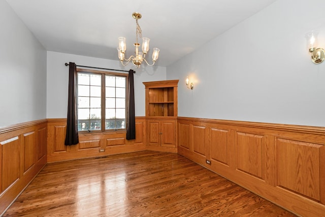 unfurnished room featuring visible vents, an inviting chandelier, wood finished floors, and wainscoting