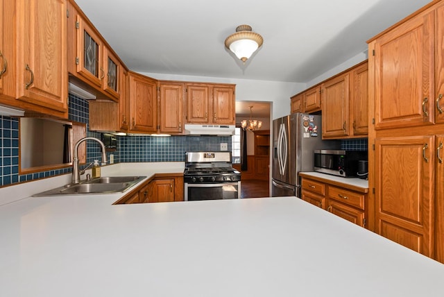 kitchen featuring under cabinet range hood, a sink, backsplash, appliances with stainless steel finishes, and light countertops