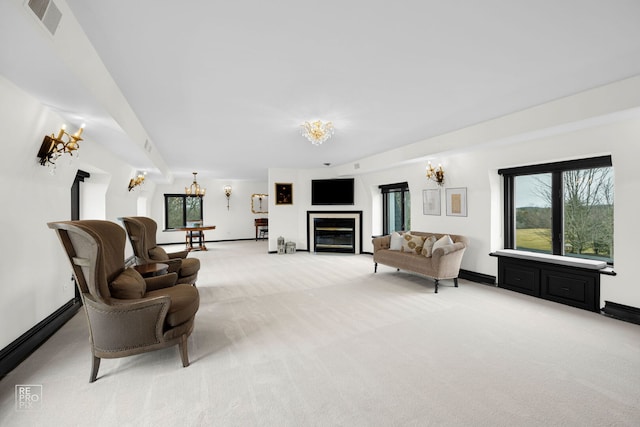 living area with light carpet, baseboards, visible vents, a glass covered fireplace, and an inviting chandelier