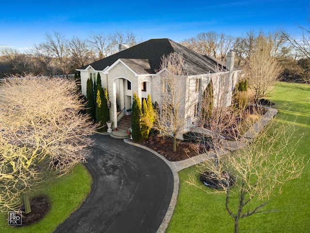 view of side of home with aphalt driveway, a yard, and a chimney