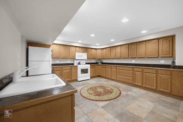 kitchen featuring recessed lighting, white appliances, a sink, brown cabinets, and dark countertops