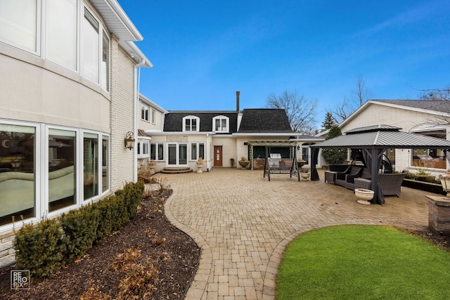 rear view of property featuring brick siding, a shingled roof, a gazebo, a patio area, and an outdoor living space