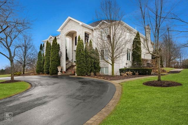 view of front of house with stone siding, curved driveway, and a front yard