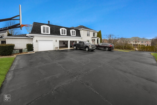 view of front of property featuring brick siding, aphalt driveway, mansard roof, and roof with shingles