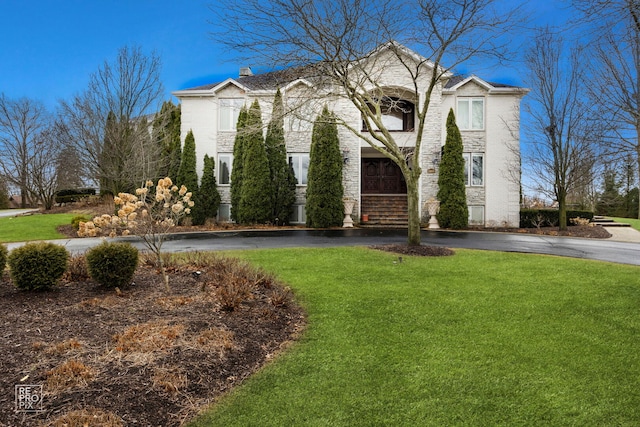 view of front of property featuring stone siding, a chimney, a front lawn, and aphalt driveway