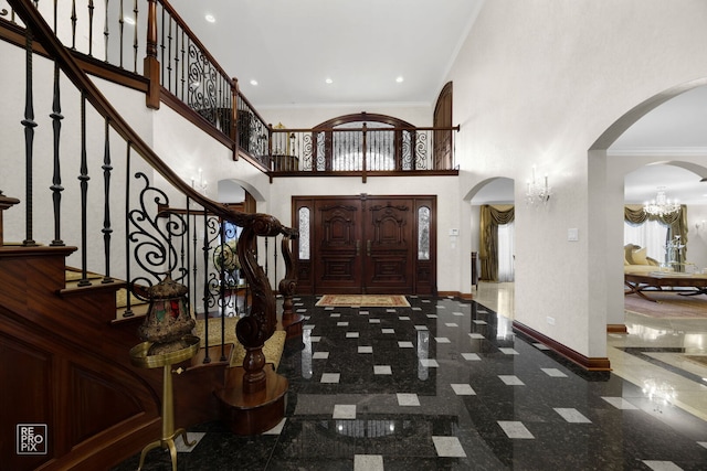 entryway with crown molding, granite finish floor, arched walkways, and baseboards