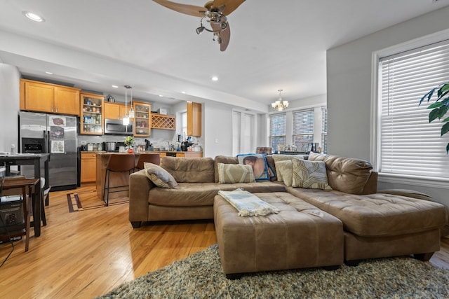 living room with light wood-style floors, ceiling fan with notable chandelier, and recessed lighting