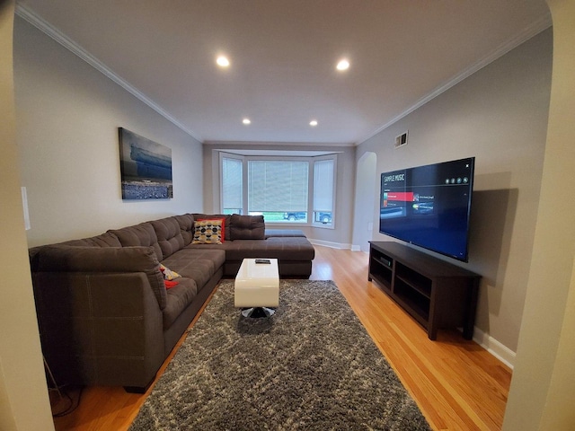 living area with baseboards, light wood-style floors, visible vents, and crown molding