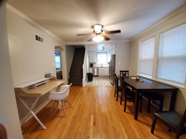 dining room featuring arched walkways, light wood finished floors, visible vents, stairway, and ornamental molding