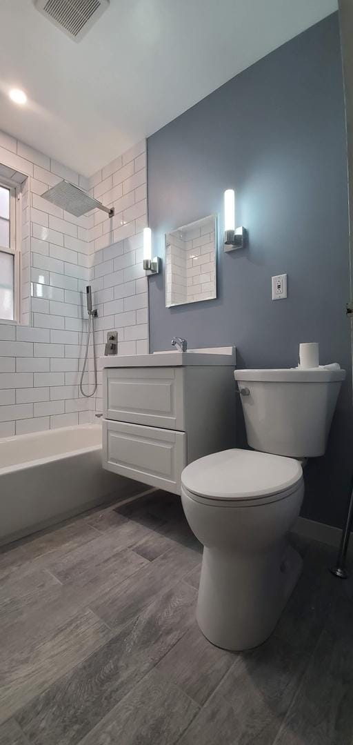 full bathroom featuring visible vents, toilet, wood finished floors, vanity, and washtub / shower combination