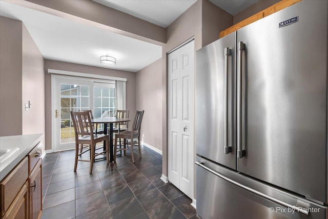 kitchen featuring light countertops, brown cabinetry, baseboards, and high end refrigerator