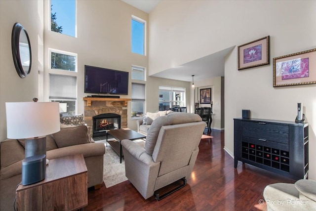 living area with a stone fireplace, baseboards, dark wood-style flooring, and a wealth of natural light